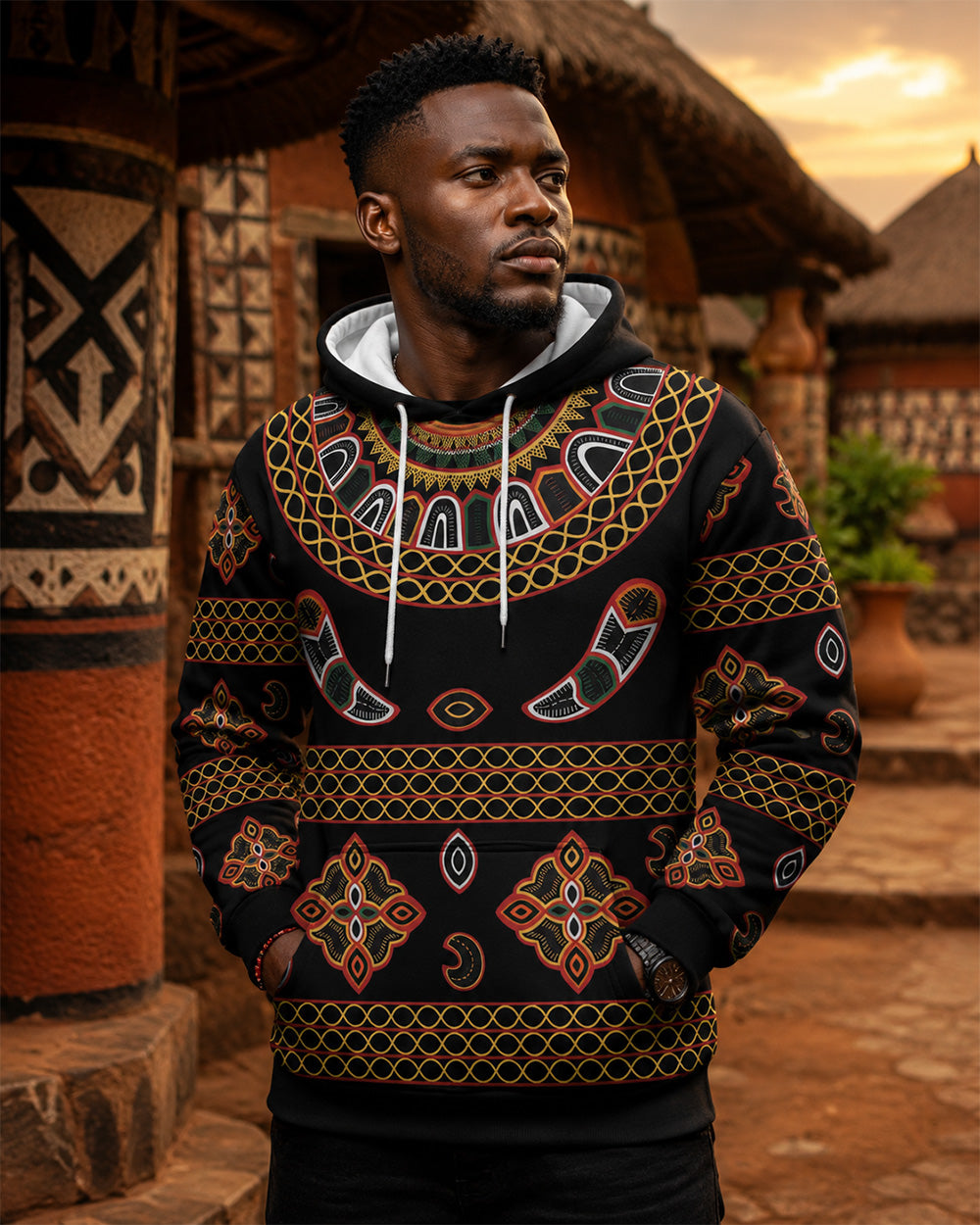 Man wearing a patterned hoodie standing in front of traditional African architecture.